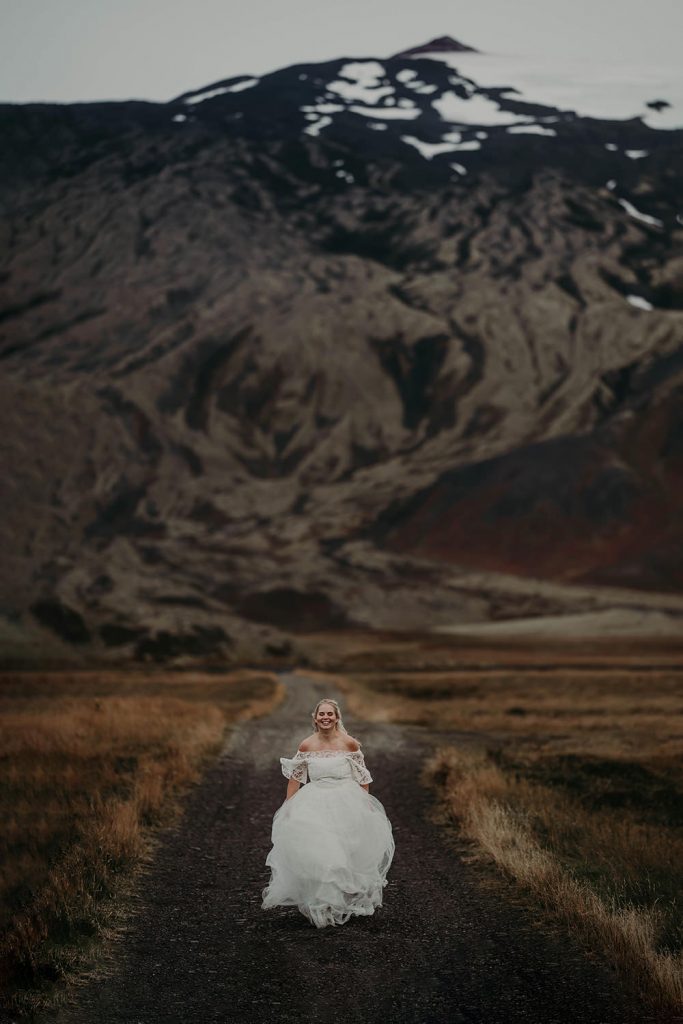 Bride running down a road with a snowy mountain behind her.