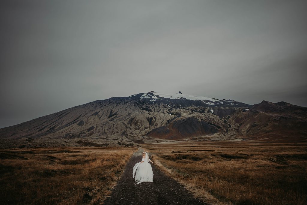 Bride running down the road with Snæfellsjökull mountain behind.