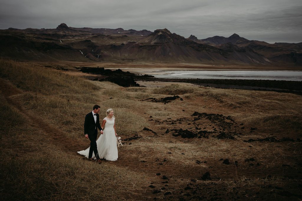 A bride and groom walking down a beach in Iceland
