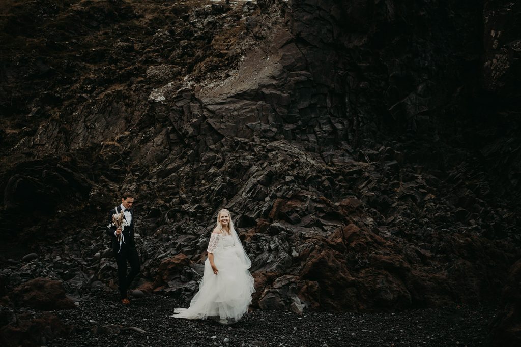 A bride and groom walking down a black sand beach